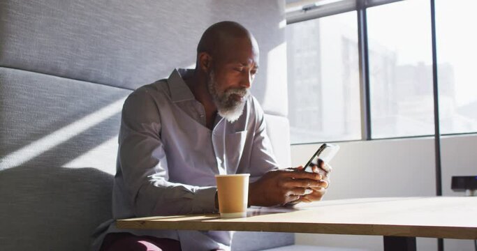 African american businessman sitting at table and using smartphone at office