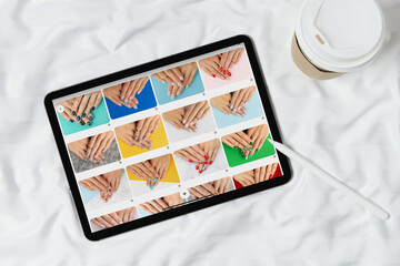 Black tablet with manicure designs on screen on white bed. Beauty salon concept