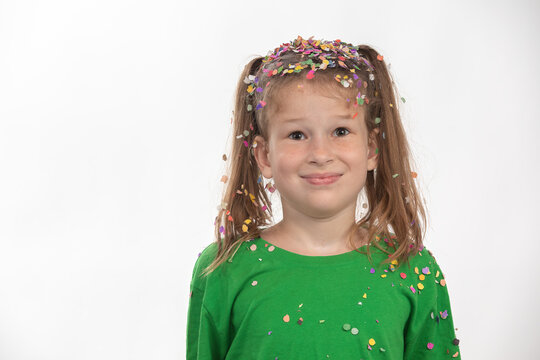Portrait of a confused child after a confetti rain with multi-colored tinsel and confetti. Having fun celebrating her birthday.