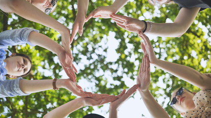 The girlfriends join their palms in a circle against the background of tree branches.
