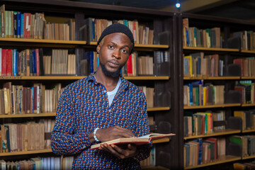 Education concept - Young handsome black student reading a book in university library.