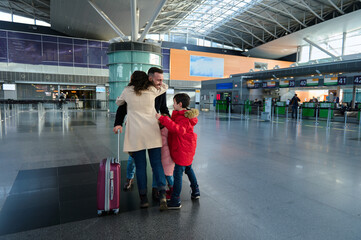 Happy young Caucasian family embraces at the arrival terminal of an international airport, enjoying...