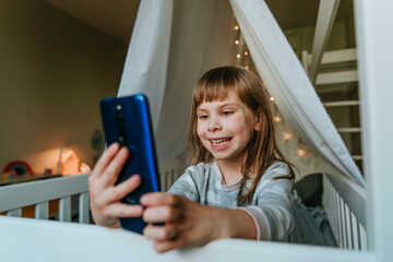 Little girl using smartphone sitting on the bed