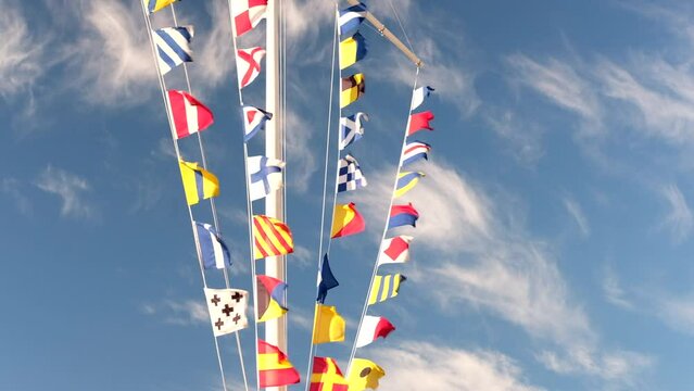 Sea ship flags on a mast waving in the wind against sunny blue sky. International maritime signal flags. Marine garland