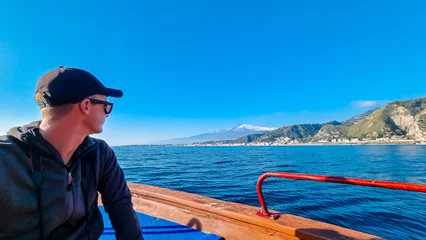 Foto op Canvas Man on touristic boat tour with panoramic view from open sea on snow capped volcano Mount Etna and the Ionian Mediterranean coastline near Isola Bella in Taormina, Sicily, Italy, Europe, EU. Cliffs © Chris
