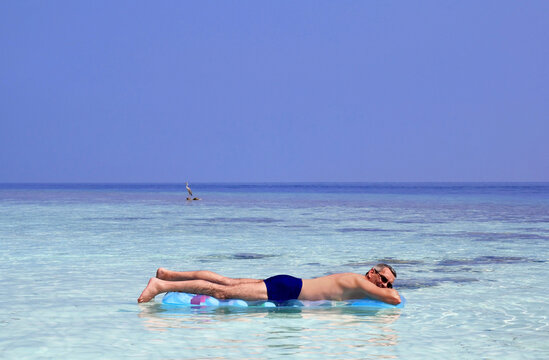 Ein Mann genießt im Urlaub auf einer Luftmatratze die Sonne und das Meer