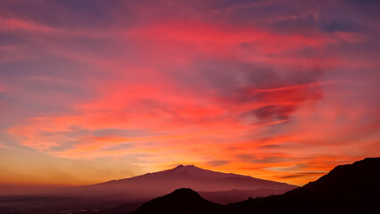 Panoramic view on silhouette of hills during twilight. Watching beautiful sunset behind volcano Mount Etna near Castelmola, Taormina, Sicily, Italy, Europe, EU. Clouds with vibrant red orange colors