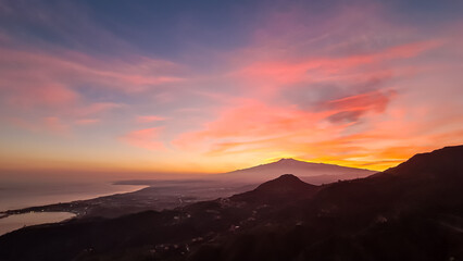 Panoramic view on silhouette of hills during twilight. Watching beautiful sunset behind volcano Mount Etna near Castelmola, Taormina, Sicily, Italy, Europe, EU. Clouds with vibrant red orange colors