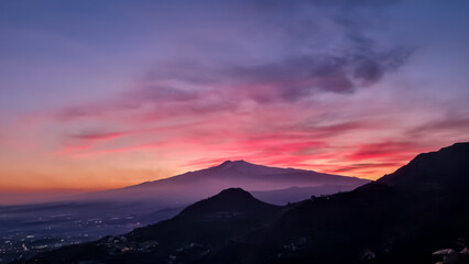 Panoramic view on silhouette of hills during twilight. Watching beautiful sunset behind volcano Mount Etna near Castelmola, Taormina, Sicily, Italy, Europe, EU. Clouds with vibrant red orange colors