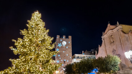Naklejka premium Christmas tree, lights and decoration at night on the main square (Piazza IX Aprile) in Taormina, Province of Messina, Sicily, Italy, Europe, EU. Happy holidays at the Mediterranean sea