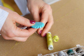 Tailor with needle in hands cutting thread. Woman seamstress at workplace. Closeup needlework