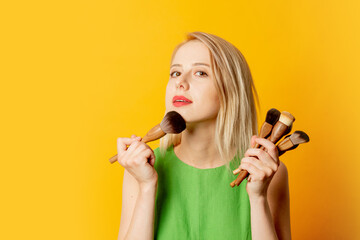 Stylish girl in green dress with makeup brushes on yellow background