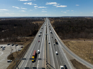 A high aerial view above a busy, multilane highway interstate on a partly cloudy, sunny day.