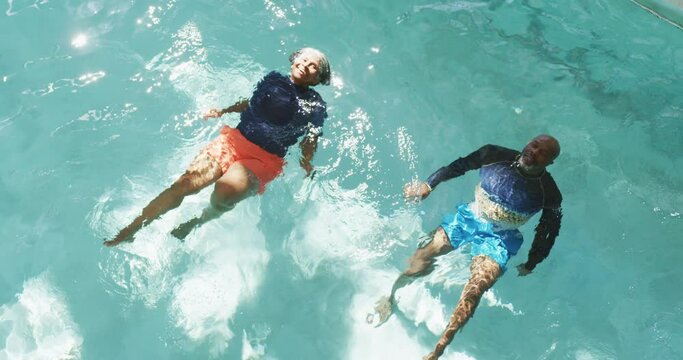 Vertical video of happy senior american african couple exercising in the pool