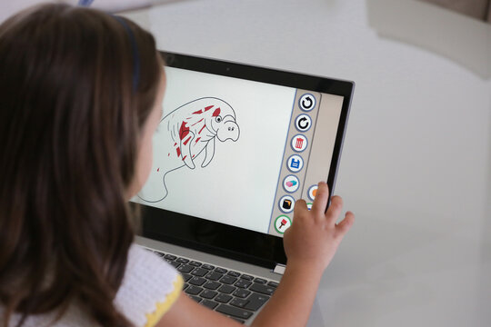 Criança brincando de jogo em frente do computador com pinturas ilustrativa.
