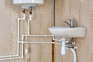 Plumbing pipeline of home water supply with electric water heater tank and sink in country house.