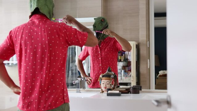  Man with dinosaur mask brushing teeth in bathroom.