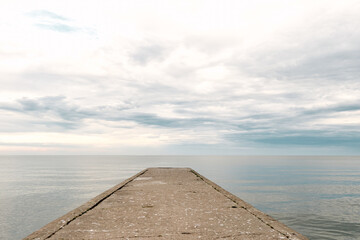 Empty concrete pier to the sea with dramatic sky and calm water, abandoned industrial jetty