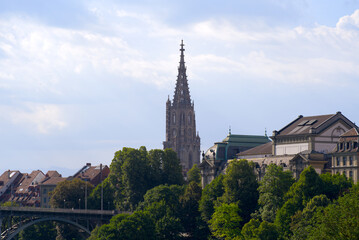 Fototapeta premium Church tower of Minster at the old town of Bern on a blue cloudy summer day with Kornhaus Bridge in the foreground. Photo taken June 16th, 2022, Bern, Switzerland.