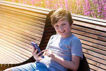 smiling schoolboy communicates in social networks in a smartphone. child watching video, playing games on a sunny day outside