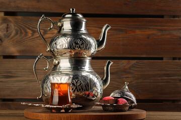 A still-life with Turkish double teapot, authentic glasses and sweets on a dark brown background.