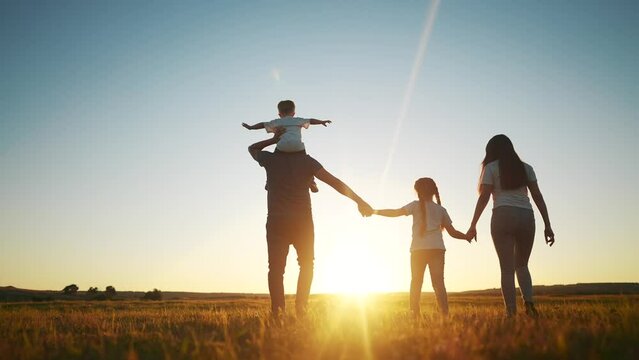 people in the park. happy family walking silhouette at sunset. mom dad and daughters walk holding hands in the park. happy family childhood dream concept. parents and children go back silhouette sun