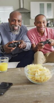 Vertical video of happy african american father and son playing video games