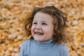 Fototapeta premium beautiful little girl playing with yellow leaves in park at fall time, autumn, card, healthy