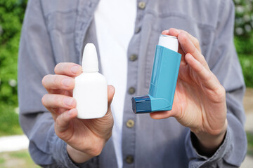 Hands of a young woman holding an asthma inhaler and nasal drops outdoors, close-up. Health and...