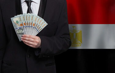 Man hand showing 100 US dollar bills on flag of Egypt background