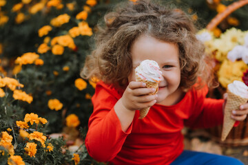 cute curly little girl eating ice cream in park fall time, autumn, card, flowers, banner