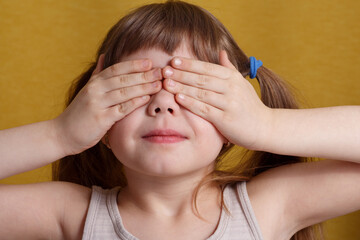 Portrait of a European little girl covering her eyes with her hands. Concept for a surprise, hide...