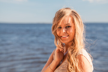 Happy pretty curly-haired woman closeup, the wind fluttering hair. Spring portrait on the beach and sea outdoors