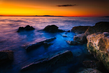 Widok skał oblewanych przez morze o wschodzie słońca przy kolorowym niebie - obrazy, fototapety, plakaty