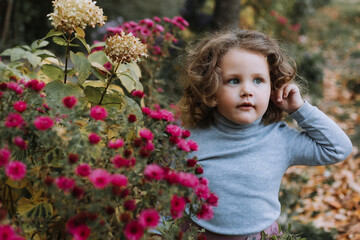 adorable curly little girl in blue shirt in park with flowers at fall time, autumn, health, card, banner