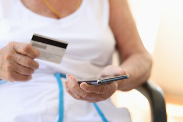 Closeup of elderly woman with hand using a smartphone and holding credit card to pay bills in online stores