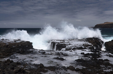 Fototapeta premium Gran Canaria, north west coast around natural swimming pools Salinas de Agaete, waves breaking against old eroded dark lava platform