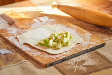 Apple filling lies on the rolled out dough. Cooking pies on the table.