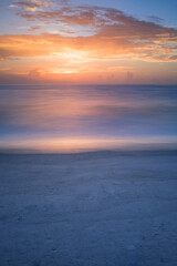 Naklejka na ściany i meble a long exposure of a calm sea reflecting a sunset with a sandy beach foreground
