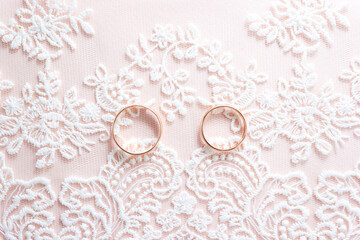 Golden rings of the bride and groom on background of white lace. Wedding card or invitation. Copy space