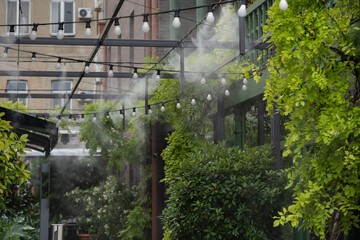 Fototapeta na wymiar Fogging outdoor cool misting system working hot summer day for terrace in cafe. Facility that lowers temperature by spraying fine mist. Air conditioning and water spray system for cooling and fog.