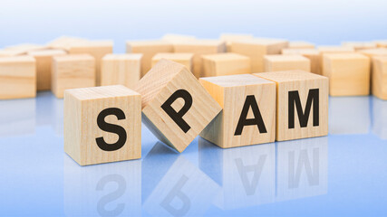 four wooden blocks with the letters SPAM on the bright surface of a blue background. the inscription on the cubes is reflected from the surface. business concept.