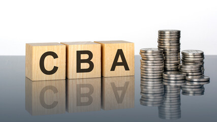 CBA - text on wooden cubes on a cold grey light background with stacks coins