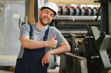 Smiling and happy employee. Industrial worker indoors in factory. Young technician with white hard hat.