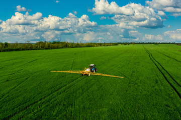 Farm machine sprayer chemicals wheat green field against the backdrop of a beautiful blue sky with clouds Modern technology of agriculture