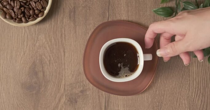 4k video, flat lay coffee white cup on wooden desktop. Espresso Hot drink health. Green plant on table in a cafe or at home. Female hand take mug of steaming coffee with drink to finish and empty cup