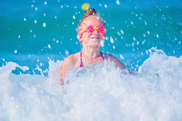 Portrait of happy child girl on breaking wave. Travel, healthy lifestyle, swimming and summer holiday concept. Horizontal image.