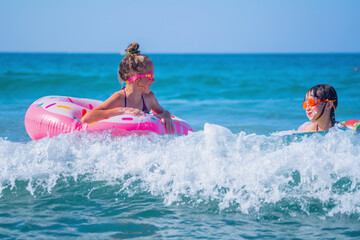 Portrait of joyful happy child girls on inflatable rings riding on breaking wave. Healthy lifestyle and summer holiday concept.