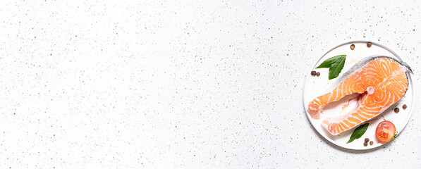 Fresh raw salmon steak with spices and herbs on the plate on white marble background. Long banner format. Healthy diet food concept.