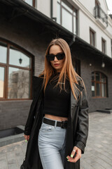 Fashionable sexy hipster woman with cool sunglasses in fashion black urban outfit with black coat,...